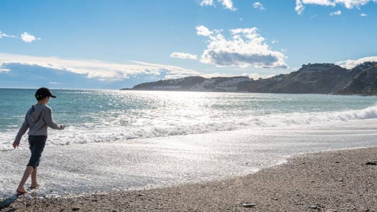 niño caminando por la orilla con un sol reluciente en la playa de almuñecar